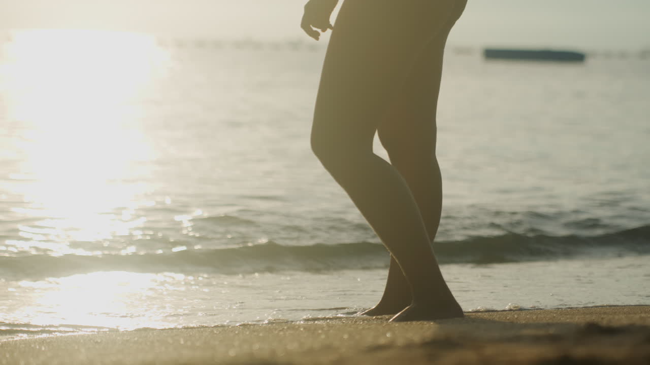 piedi che camminano lungo la riva nella luce dorata, primo piano di piedi che premono la sabbia bagnata, onde delicate che creano schiuma, impronte che appaiono e svaniscono, ritmo del cercatore di conchiglie e movimento consapevole che radica