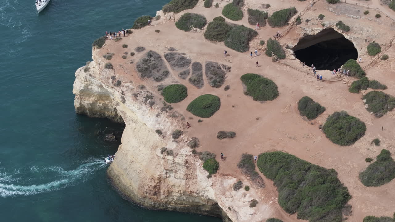 Aerial drone view of the Benagil Sea Cave and Atlantic Ocean coastline in Benagil, Algarve, Portugal, Europe. Boats and people sightseeing, mass tourism concept