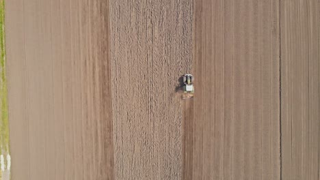 Top-down-aerial-of-tractor-plowing-an-empty-field-and-kicking-up-dust-and-dirt