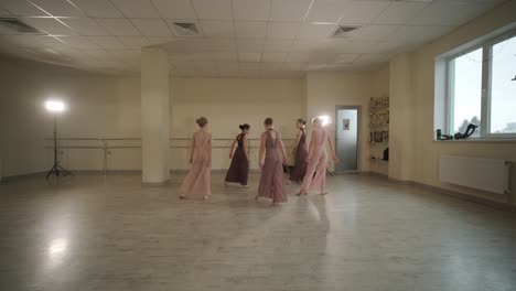 a group of young ballet students in black dancewear practicing positions in a spacious ballet studio with wooden flooring and wall-mounted barres. focused expressions and synchronized movements.