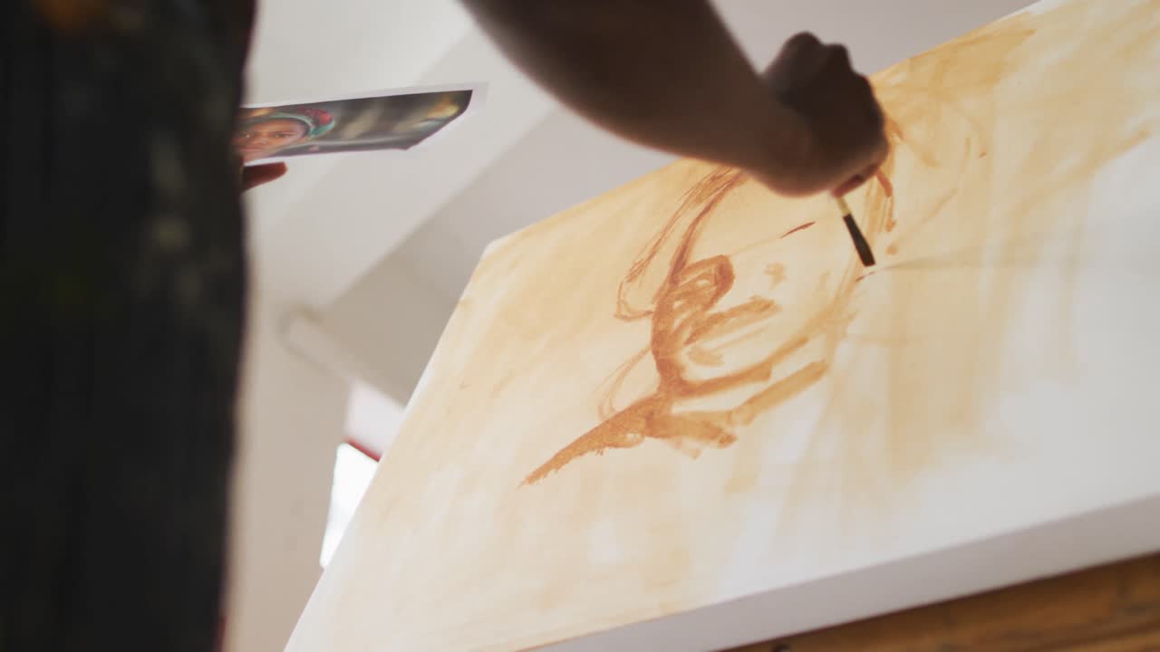 pintor afroamericano de sexo masculino pintando a partir de una fotografía en lienzo en el estudio del artista