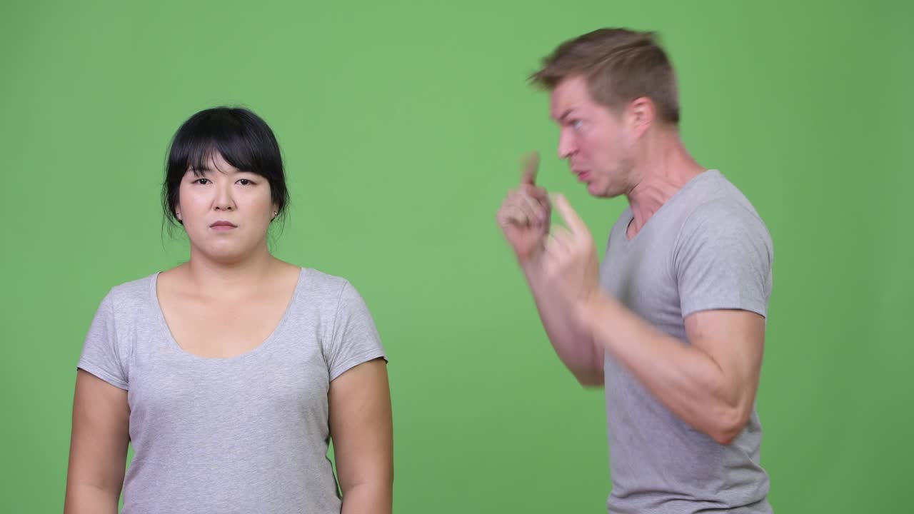 Young angry man talking to calm overweight Asian woman