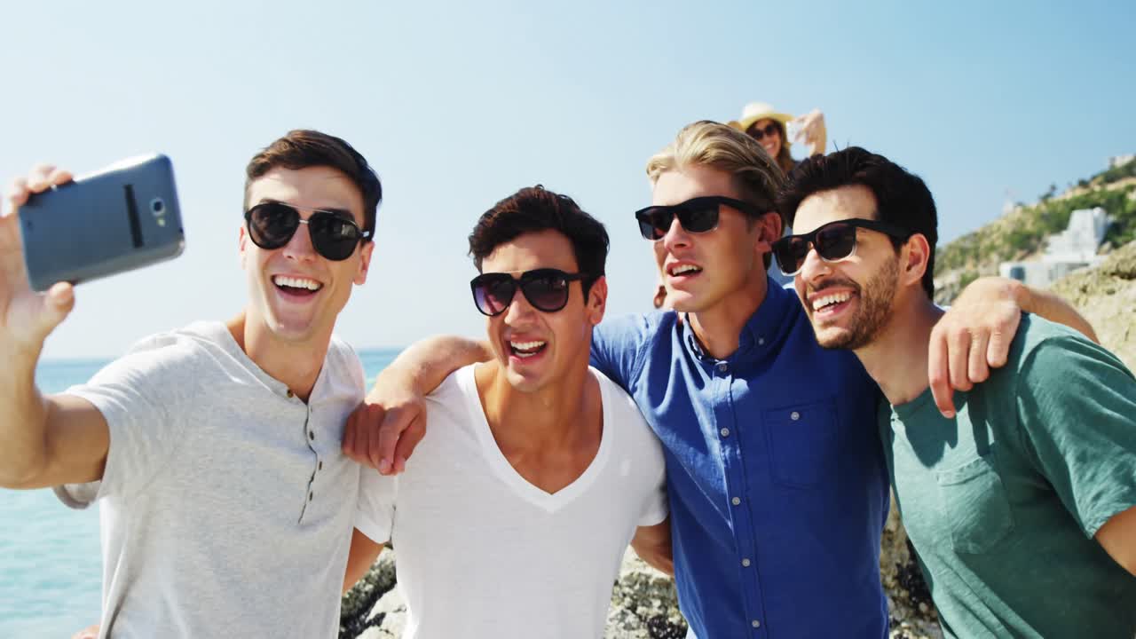 친구 들 이 해변 에서 휴대폰 으로 셀카 를 찍고 있다