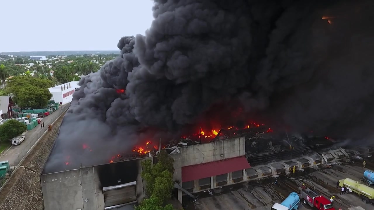 Vigili del fuoco che cercano di spegnere un grande edificio in fiamme con denso fumo nero