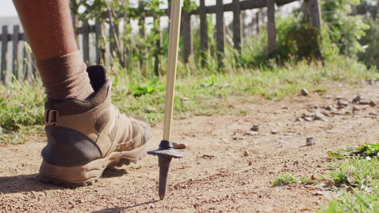 Low section of senior african american man hiking with trekking poles on sunny day, slow motion