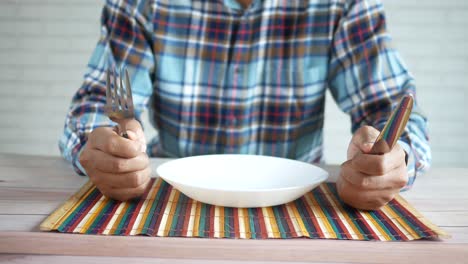 persona sentada en una mesa con un plato vacío y cubiertos