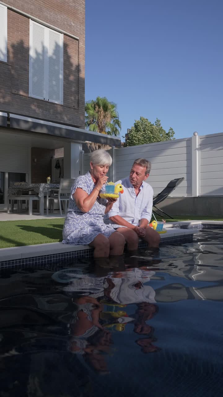 Una coppia di anziani si rilassa a bordo piscina con dei paperelle di gomma
