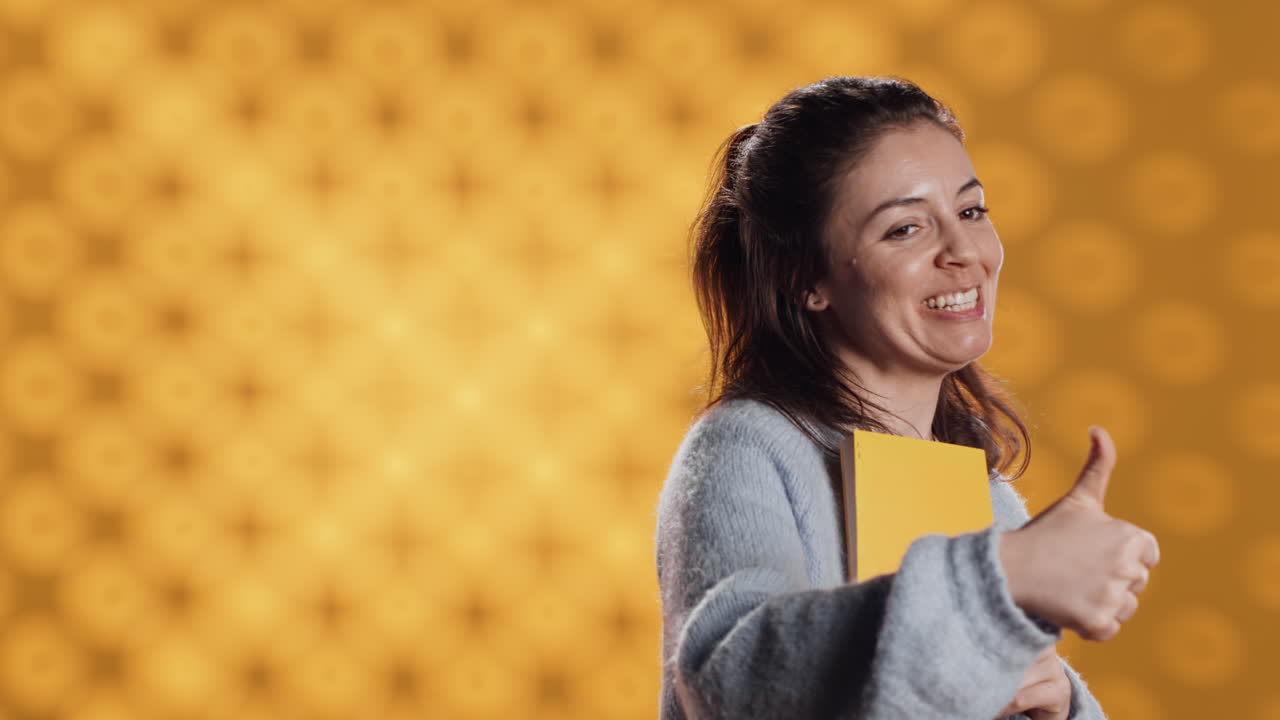 mujer feliz delirando sobre libro increíble, mostrando pulgares hacia arriba, fondo de estudio