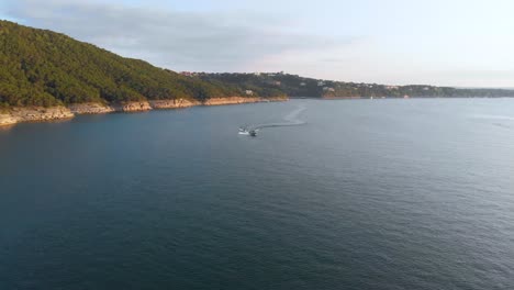 Head-on-shot-of-a-boat-pulling-a-wakeboard-with-the-cliffs-of-lake-travis-in-the-background