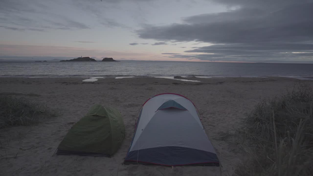 Wild camping in a beach in scotland. Two tents in fornt of the sea during sunrise time. Wide angle shot