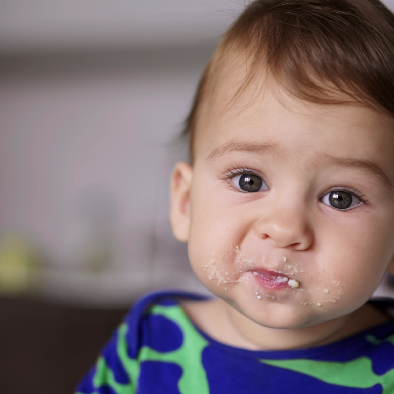 Beautiful grey-eyed baby boy eating dairy indoors. Cute Caucasian kid eating well from spoon. Close up