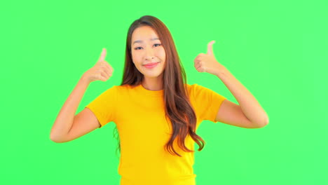녹색 배경을 배경으로 한 젊은 여성이 성공을 위해 엄지손가락을 치켜들며 미소 짓고 있습니다.