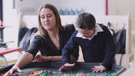 female teacher and down syndrome boy at a sensory play tub in a primary school classroom, front view