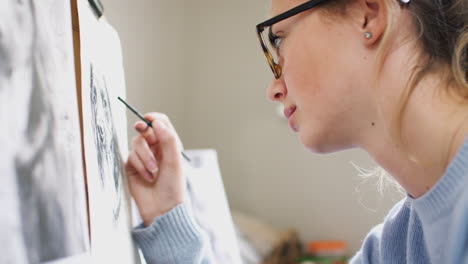 close up of artist sitting at easel drawing picture of dog in charcoal from photograph