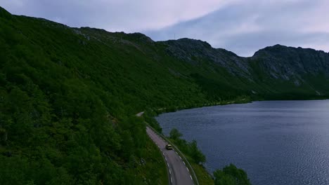 在挪威北部的洛福<unk> (lofoten) 綠色森林樹林景觀中追蹤一輛金色汽車的空中拍攝,道路向努斯菲奧德 (nusfjord) 和山脈<unk>曲,夏天可以看到藍湖景觀.