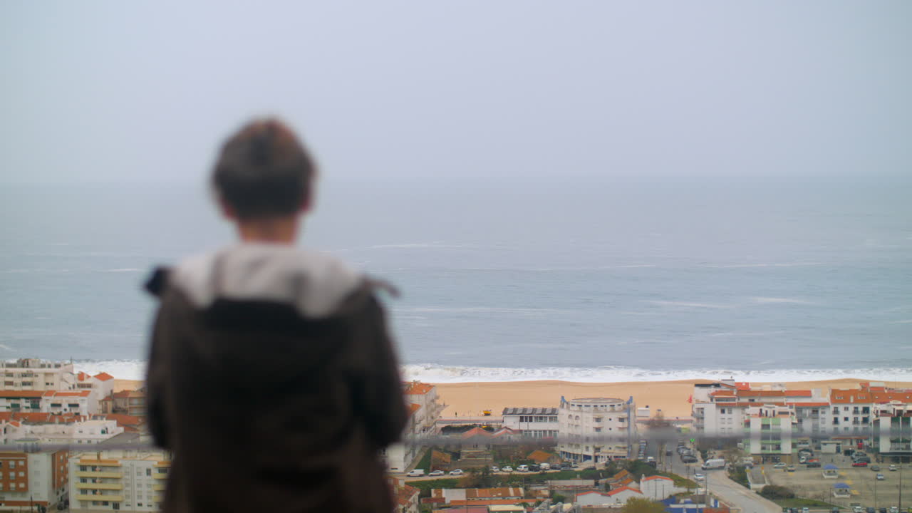 포르투갈 나자레의 해안가에 있는 호텔에서 바다를 바라보는 십대 소년