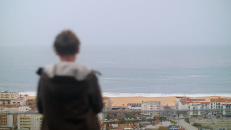 teenager boy looking at ocean from the hotel on the coast in nazare portugal