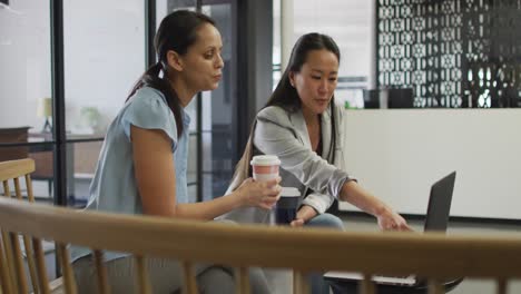 two diverse businesswomen with coffee working on laptop in office