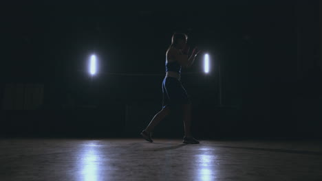 Boxer-woman-in-red-bandages-on-the-hands-of-and-blue-t-shirt-conducts-battle-with-of-practicing-the-speed-and-technique-strikes-hands.-Camera-movement-side-View.-Steadicam-shot