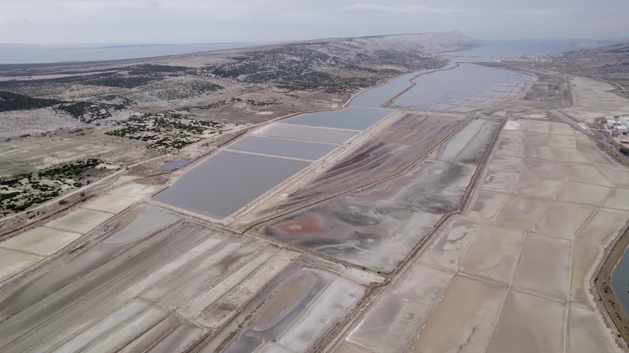 Coastline and salt flats surrounded by hills and reservoirs seen from above, Pag, Croatia