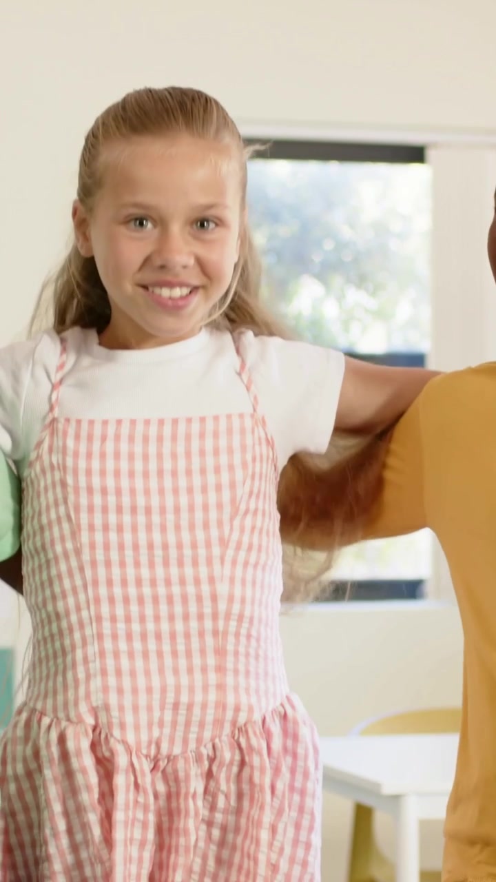 Vertical video: Linking arms as peers form for pose, youth smiling and shifting in school, pinafore