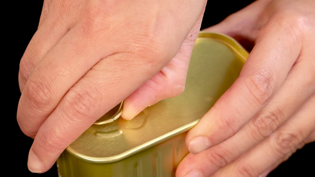 A person’s hands open a rectangular pull-tab can, demonstrating the step-by-step process under bright, even lighting with a close-up perspective