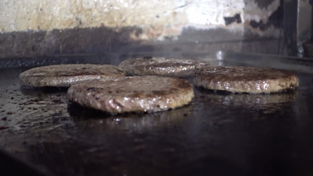 Nærbillede af bøfburgere, der steger på en åben grill i et køkken