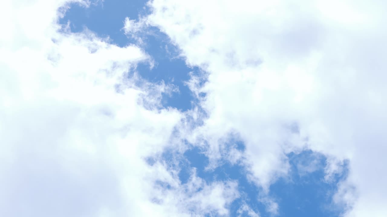 Céu azul brilhante com nuvens brancas fofas e suaves, criando uma atmosfera serena e tranquila durante o dia. A luz do sol realça essa cena natural com uma vista clara e ampla em um dia ensolarado