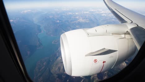 wide shot of plane engine and wing in flight with mountains and lake in background