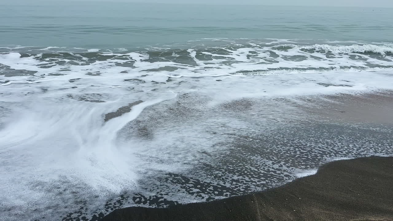 Onde che si infrangono su una spiaggia sabbiosa con schiuma durante una giornata nuvolosa vicino alla costa