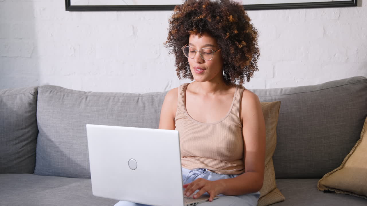 Smiling woman using laptop on couch at home, enjoying relaxed work environment, copy space