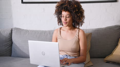 smiling woman using laptop on couch at home, enjoying relaxed work environment, copy space