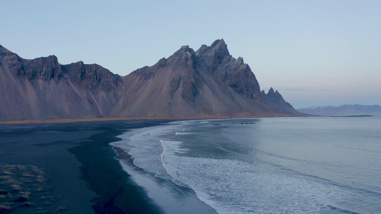 Luftoptagelse, der bevæger sig baglæns, af den enorme Vestrahorn-bjergkæde ved den sorte basaltstrand på Island.