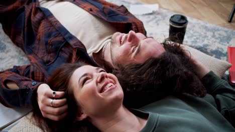 happy brunette girl lies on the floor on a pillow with her boyfriend with curly hair and touches her hair. a girl and a guy lie on the floor head to head and touch each others hair