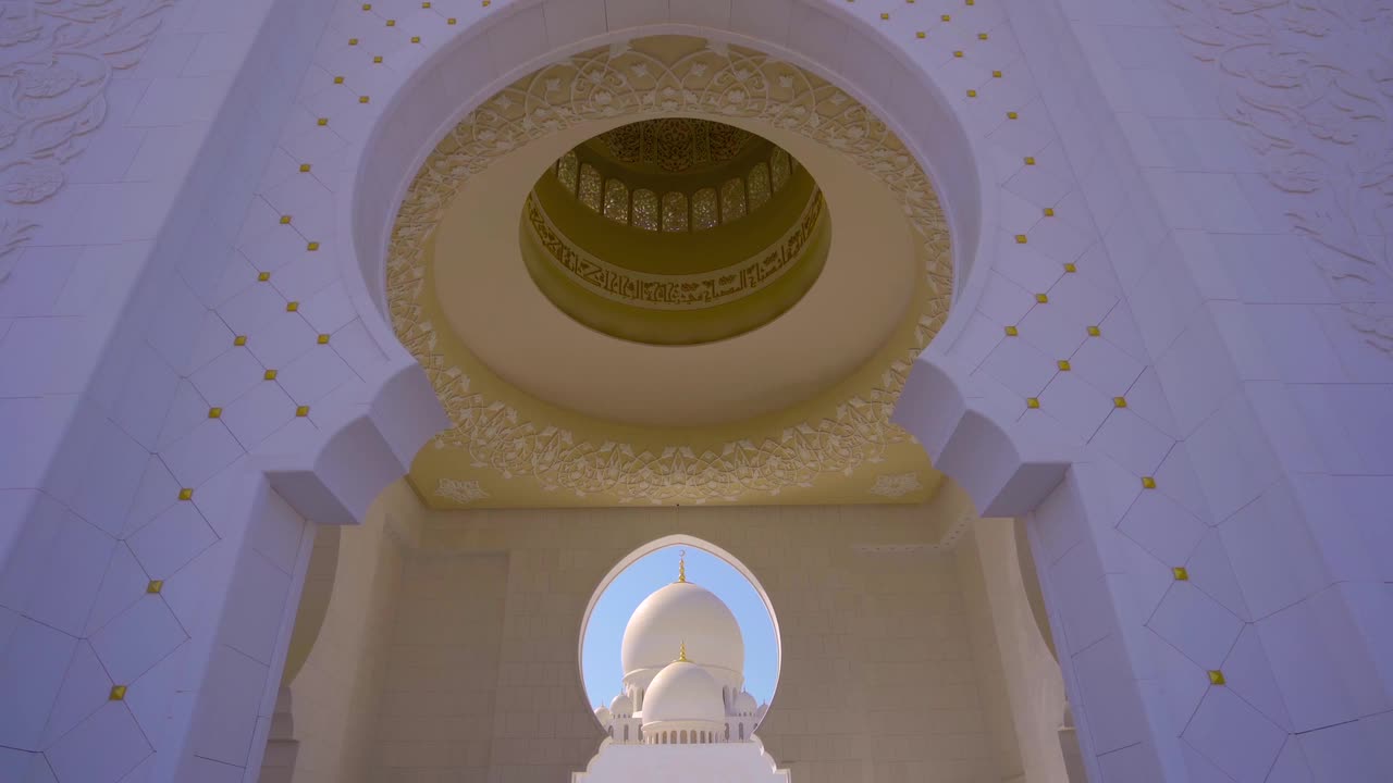 Una splendida vista grandangolare dell'interno della Grande Moschea Sheikh Zayed, che mette in risalto l'intricata calligrafia dorata sulla cupola e gli archi maestosi. La luce del sole illumina la scena serena