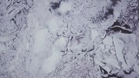 Top-down-drone-shot-flying-above-a-snowy-river-with-big-ice-chunks-during-a-winter-storm-in-New-England