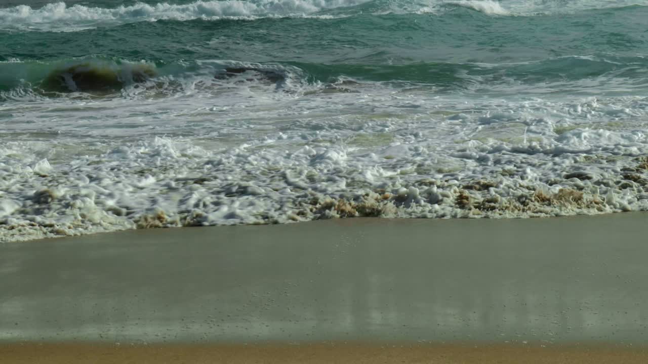 Slow motion shot of waves gently breaking on a sandy bank, capturing the serene motion and the beauty of the shoreline.