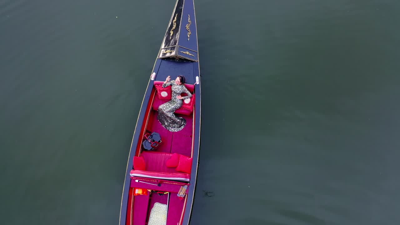 Beautiful model in gondola. Woman enjoys vacation while floating in a boat on water. Luxury woman sailing in gondola. Aerial view.