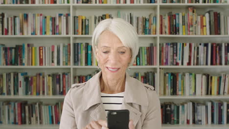 Portrait-elderly-woman-student-using-smartphone-research-bookshelf-library-university