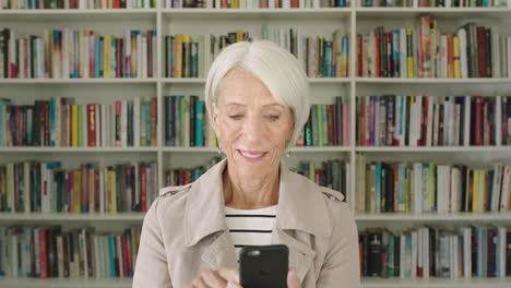 retrato mujer anciana estudiante usando teléfono inteligente investigación estantería biblioteca universidad