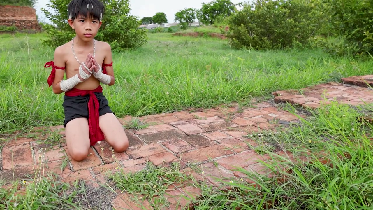 Ragazzo asiatico esegue un rituale di preghiera tradizionale in costume da arti marziali tra le rovine di un tempio storico all'aperto
