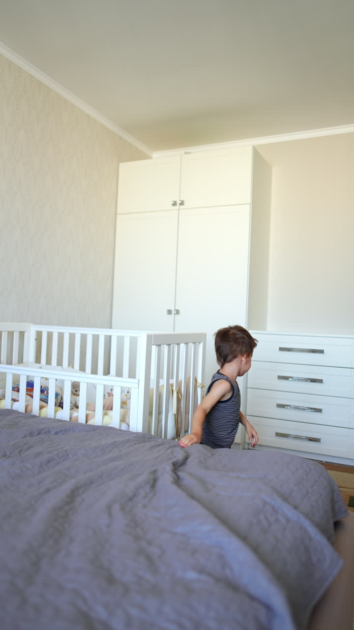 Energetic Caucasian toddler baby jumps on a big bed. Kid climbs off the bed and walks away. Fun at home. Vertical video.