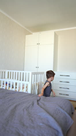 energetic caucasian toddler baby jumps on a big bed. kid climbs off the bed and walks away. fun at home. vertical video.
