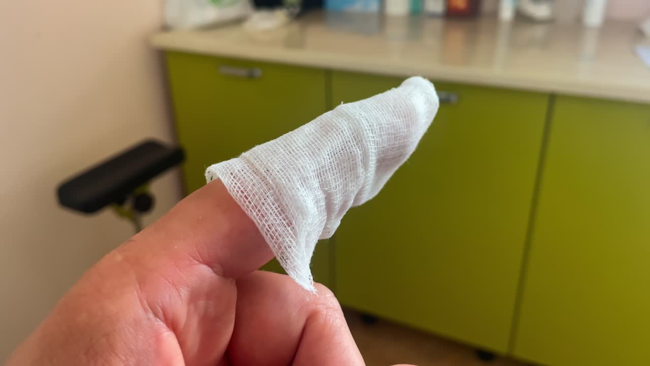 Person shows bandaged finger tip after stitches treatment with visible dressing on skin