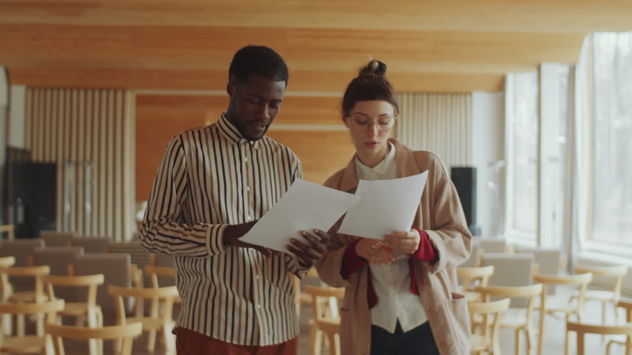 Man and Woman Discussing Documents in Auditorium