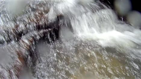 Agua-Corriendo-Sobre-Rocas-Y-Salpicando-La-Lente-De-La-Cámara