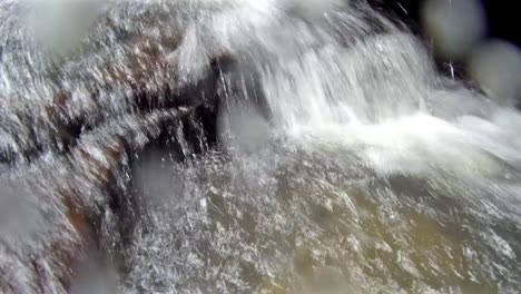 agua corriendo sobre rocas y salpicando la lente de la cámara