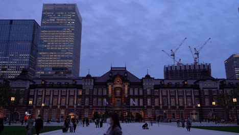 famous tokyo station at night with commuters moving around and skyscrapers in background - wide frontal view