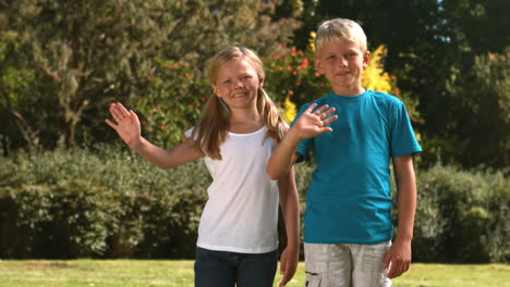 cheerful siblings waving together in their garden