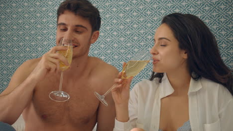 Playful-couple-celebrating-with-champagne-indoors.-Romantic-couple-flirting-bed.